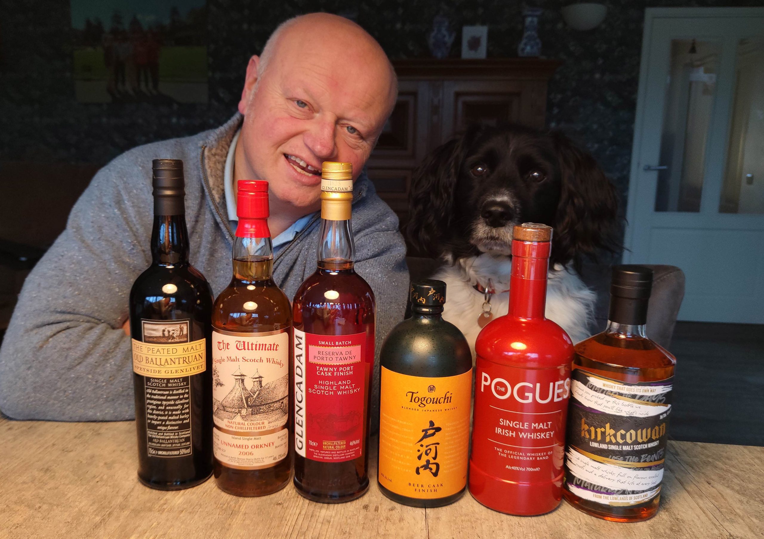 line-up van rechts naar links: Kirkcowan Lowland single malt Scotch The Pogues single malt Irish distilled at West Cork Distillers Togouchi Blended Japanese Beer Cask Finish Glencadam Small Batch Tawny Port finish scotch The Ultimate Unnamed Orkney 17yo Old Ballantruan peated malt Achter de zes whiskyflessen whiskyteacher Henri Goossen en the whiskydog Scotty, een friese Staby.